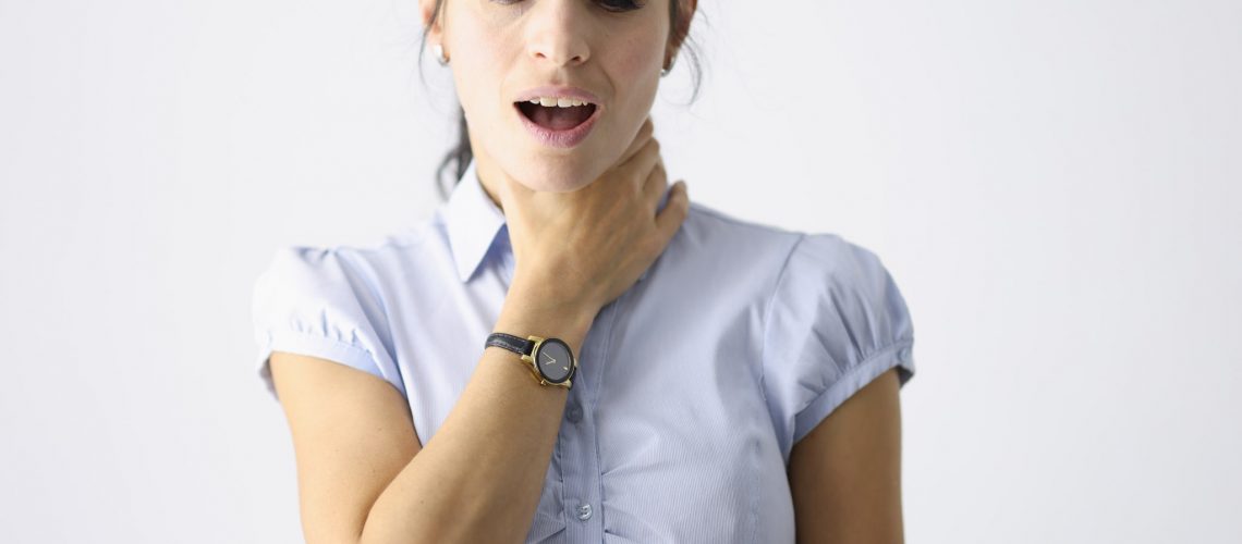 Frustrated woman holds her throat with her hand and coughs. Respiratory tract disease concept