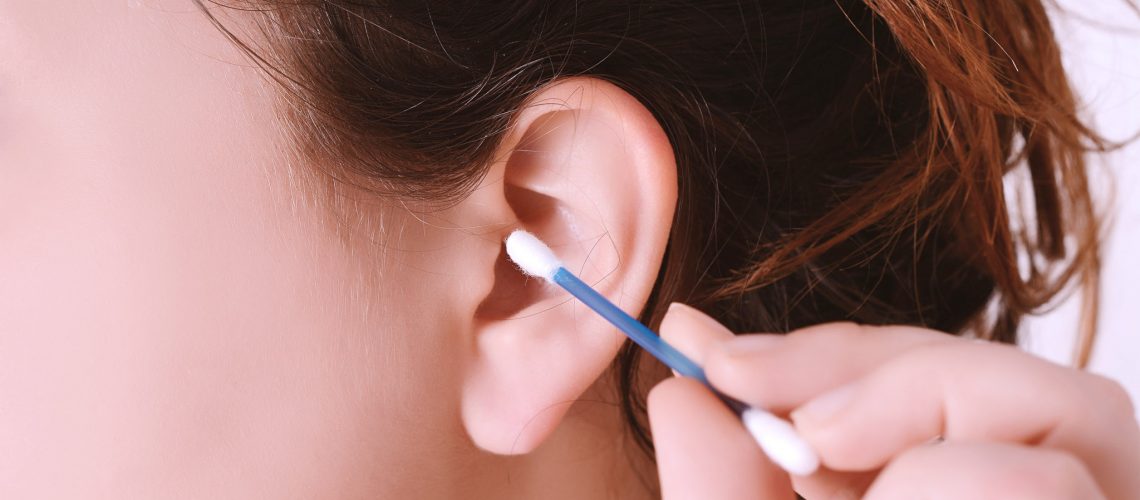 Close up of woman cleaning her ear with a cotton swab. Isolated on white background