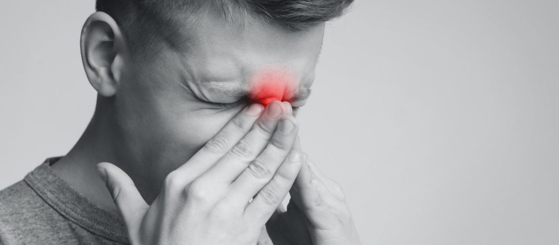 Frustrated man suffering from sinus pressure, touching his nose with closed eyes, free space